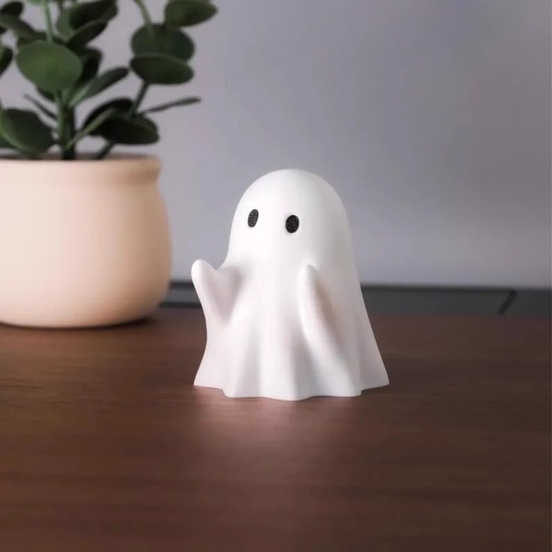 白色可爱小幽灵双手托举的小笔架在桌面上